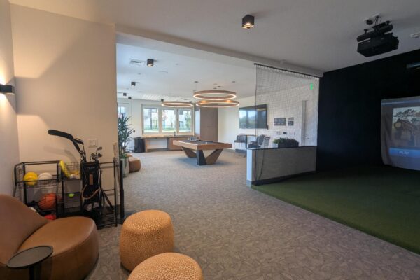 Bright, contemporary recreation room with a billiards/pool table, circular pendant lights, and comfortable seating near windows and a turf area.