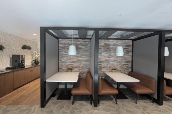 Modern cafe seating with black-framed booth dividers, white tables, and brown leather benches under white pendant lights.