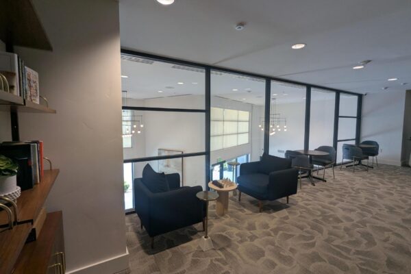 Modern lounge area with navy chairs, round tables, and glass divider separating seating from the hallway